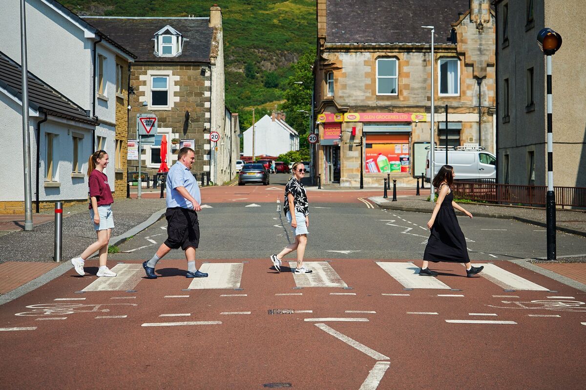 Four pedestrians, made up of colleagues and people supported, crossing a quiet town street using a zebra crossing on a sunny day